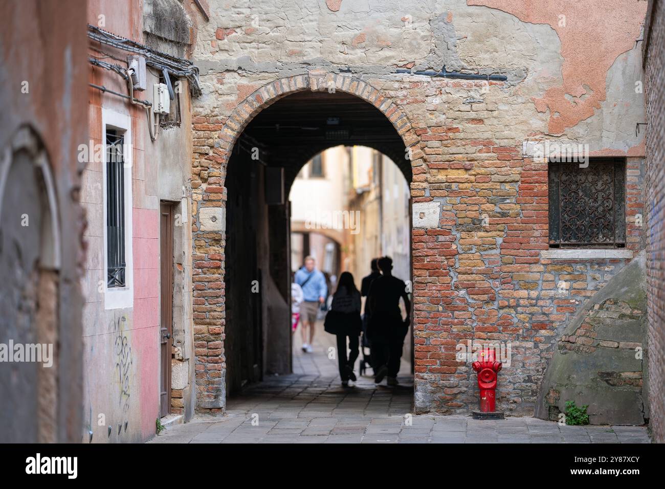 Strada con arco nella storica città italiana, Venezia. Vicolo stretto di Venezia con un vecchio arco in mattoni intemprati che conduce ad un altro passaggio. Foto Stock
