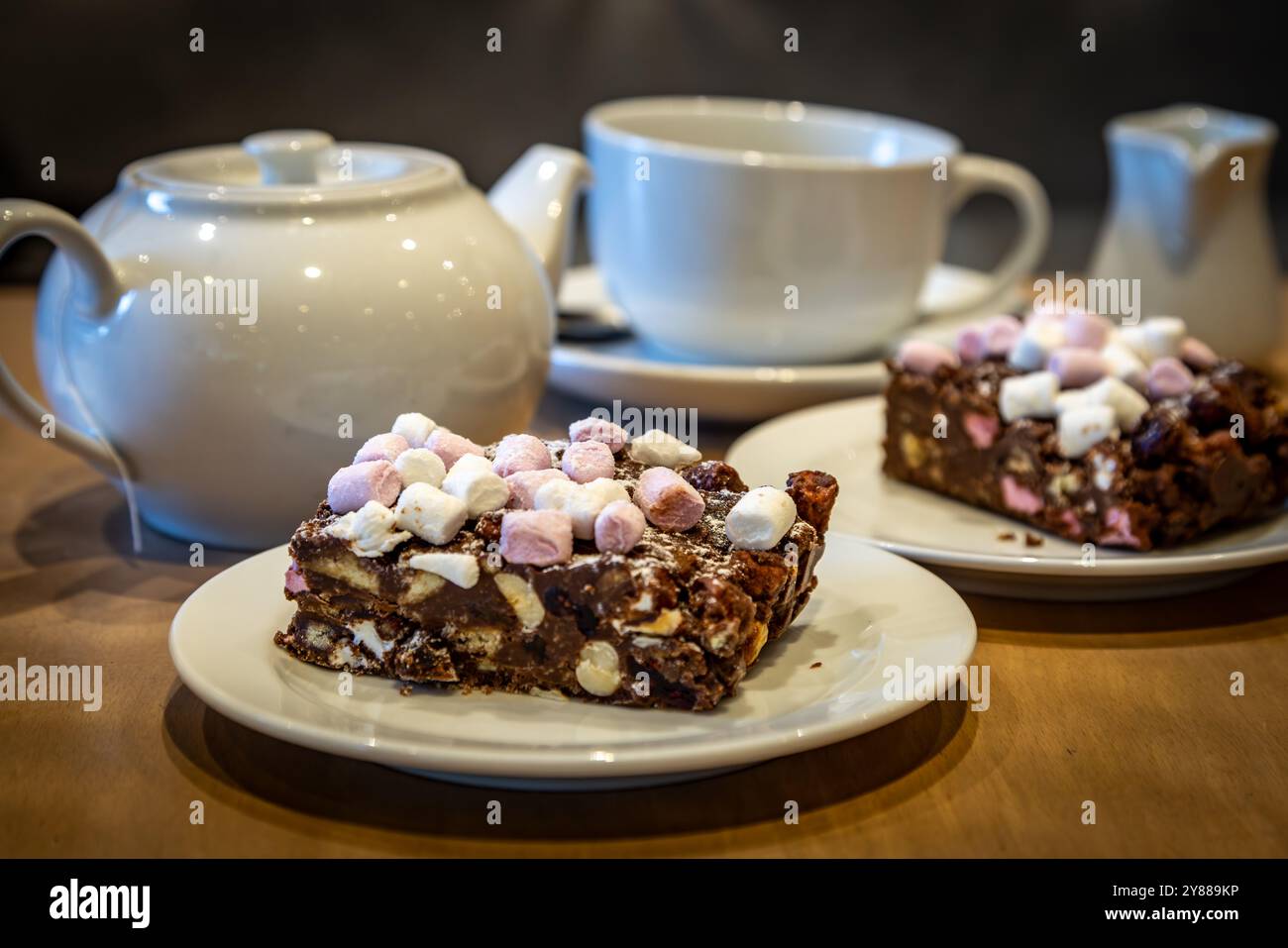 Un primo piano di una fetta di deliziosa torta stradale rocciosa, con una teiera e una tazza dietro Foto Stock