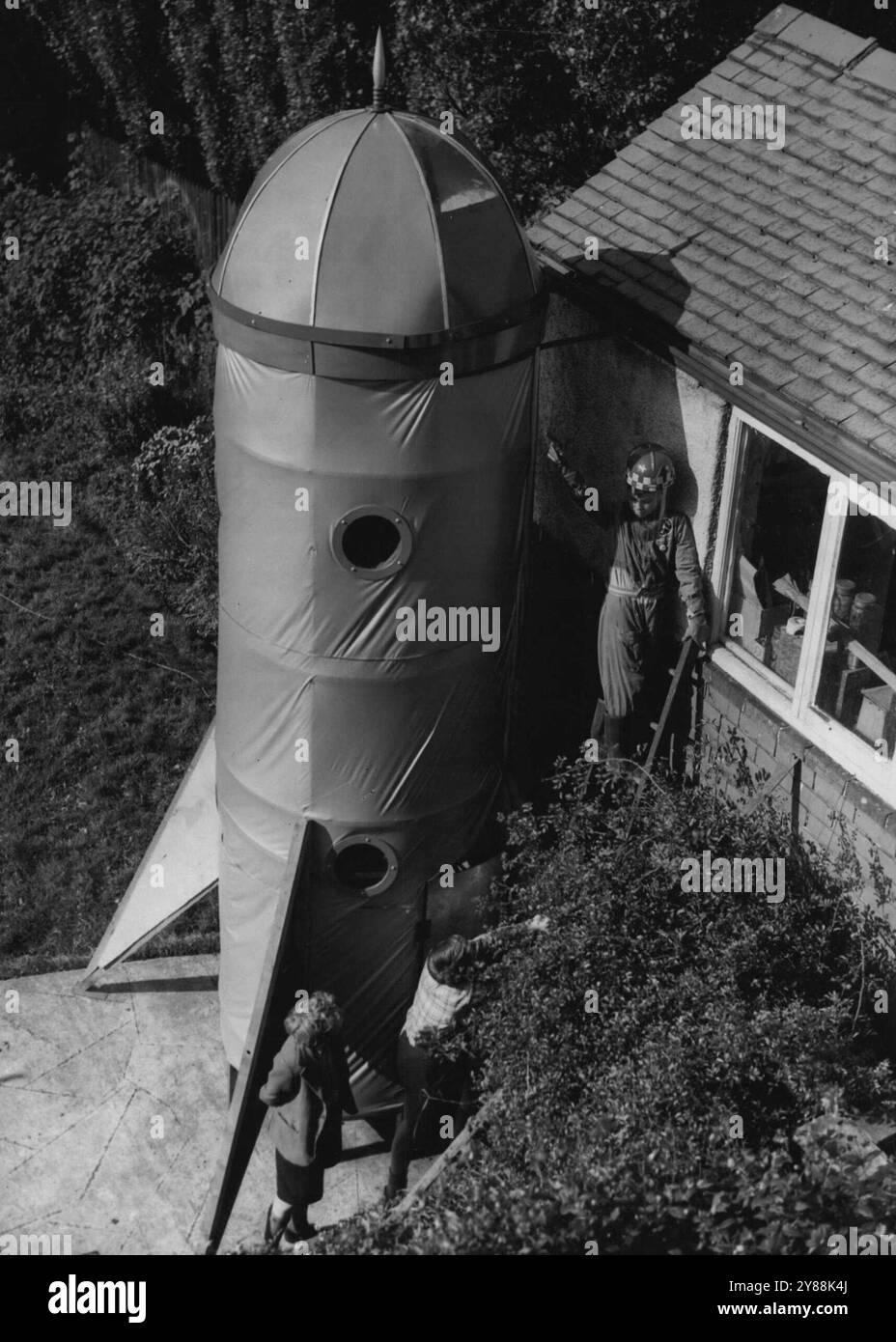 La nave spaziale "Lunar Belle" si avvicina al completamento -- il 10enne Jimmy Maxwell sottolinea uno dei "dettagli tecnici" della sua nave spaziale, dalla cima di una scala nel suo giardino. La nave spaziale "Lunar Belle", che ha impiegato tre mesi per costruire finora, è quasi finita. Il progettista, il signor S.D. Maxwell, di Sheffield, deve solo riparare l'illuminazione elettrica e un motore... Per gli effetti. Mr. Maxwell l'ha costruita nel suo giardino posteriore per suo figlio di 10 anni Jimmy, che sarà il pilota e il capitano della sua nave. La "Lunar Belle" è realizzata in legno, legno e tessuto a palloncino e ha tre piani. Ottobre Foto Stock