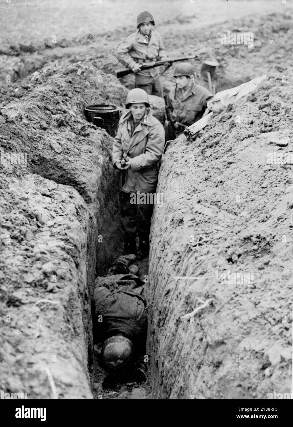 Il nono esercito degli Stati Uniti lancia Surprise Assault -- la fanteria del nono esercito degli Stati Uniti sgombra una trincea catturata dove i soldati nazisti morti giacciono rivolti verso il basso sul suolo del Reich. Le forze della nona Armata, che furono spostate segretamente attraverso la Francia, il Belgio e l'Olanda e poste su un fronte tra Geilenkirchen ed Eschweiler, in Germania, catturarono cinque città tedesche nelle prime ore di combattimento dopo che una nuova offensiva fu lanciata il 16 novembre 1944. Da sei eserciti alleati che si avvicinano al Reich. 17 dicembre 1944. (Foto di Keystone Photo). Foto Stock