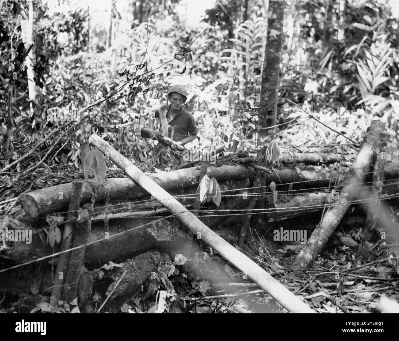 Il PFC Jerry Pezzeninti di Victor, New York, membro della 1st Cavalry Division, ispeziona una posizione di cannone giapponese sull'isola di Los Negros all'interno del Admiralty Group. La pesante costruzione di tronchi è tipica della maggior parte delle pillbox e delle postazioni delle pistole utilizzate nella guerra nella giungla. Le linee telefoniche in primo piano sono state inserite tra le nostre posizioni da Signalmen della 1a Divisione di cavalleria. 22 marzo 1944. (Foto di USA Signal Corps Photo) Foto Stock