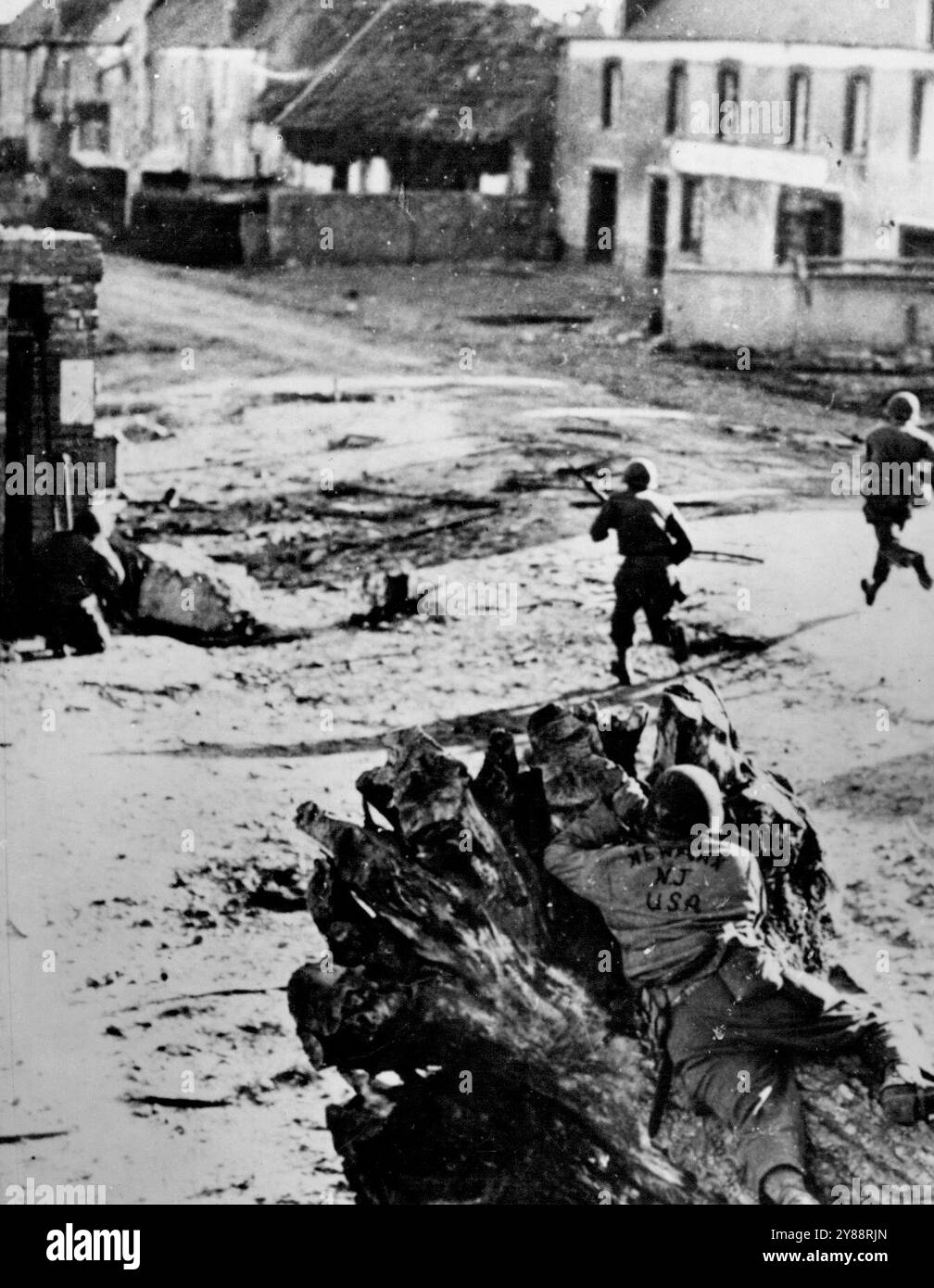 Soldati statunitensi scacciano i tedeschi da ***** Coperto da un compagno di tiro acuto sparato in un ceppo di alberi in primo piano, la fanteria degli Stati Uniti carica una strada nel villaggio di Sainteny in Normandia. L'americano in primo piano ha decorato la sua giacca con il nome della sua città natale, New York, nello stato orientale dei New German nei sanguinosi combattimenti che culminarono nella liberazione di St Lo dagli Alleati il 18 luglio 1944. 13 settembre 1944. Foto Stock