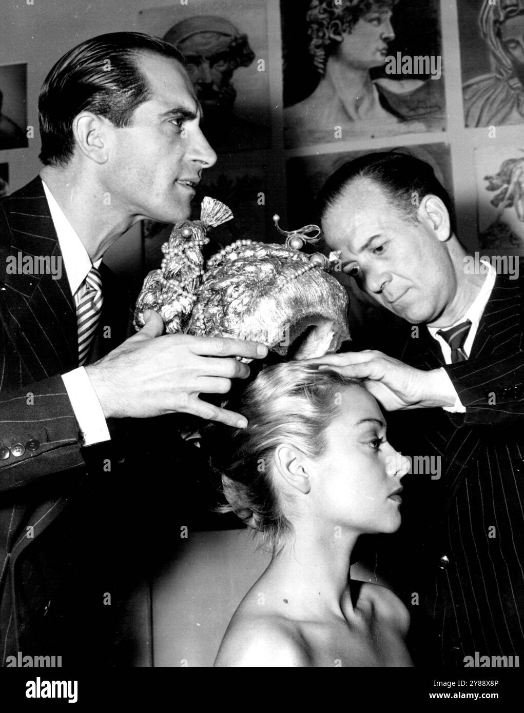 Un parrucchiere parigino di nome Antonio ha creato alcuni coiffures di Raffia che lui stesso definisce "fuori da questo mondo". La fama di Antonio iniziò diversi anni fa quando progettò un parrucchiere per la Duchessa di Windsor. Ora, nei suoi coiffures da champs che si adattano ai dolcetti di Milady come i cappelli. Qui, Antonio, (a sinistra) e un assistente montano una delle sue creazioni su un modello. Questo elegante numero si chiama "Simonetta Vespucci" e si ispira a un vecchio dipinto italiano. 19 marzo 1947. Foto Stock