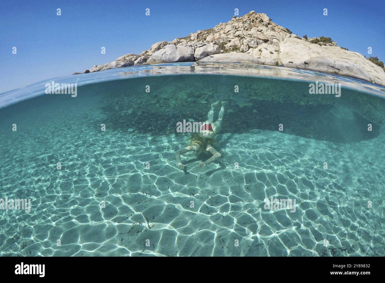 Una giovane donna nuota sul fondo di una spiaggia esotica con vista a metà sott'acqua Foto Stock
