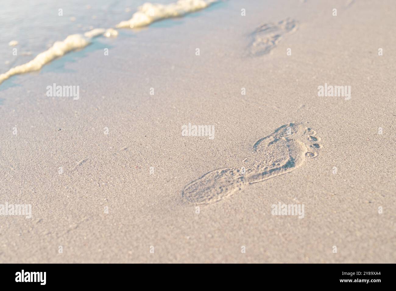 Vista ad alto angolo delle impronte sulla spiaggia sabbiosa in riva al mare durante il tramonto, spazio copia Foto Stock