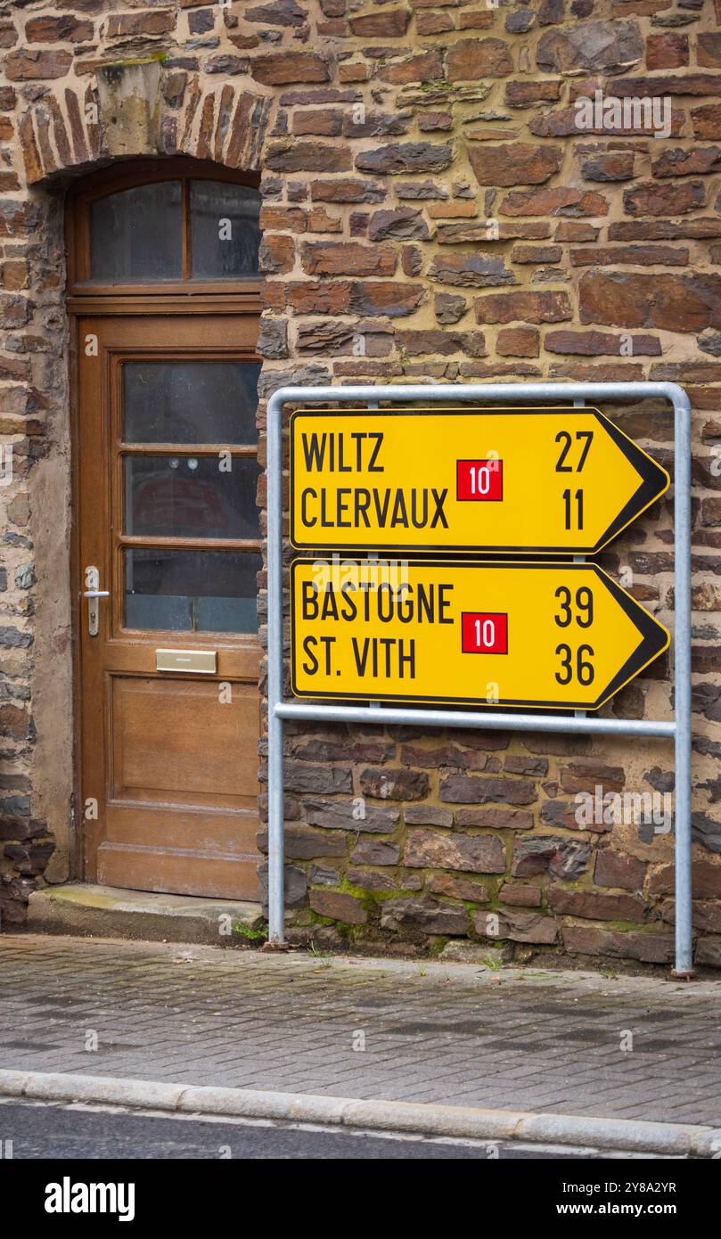 Segnale stradali gialli per Wiltz, Clervaux, Bastogne e St. Vith, con un indicatore del Lussemburgo e un cartello per sentieri, sono montati su un edificio in pietra, Lussemburgo. Foto Stock