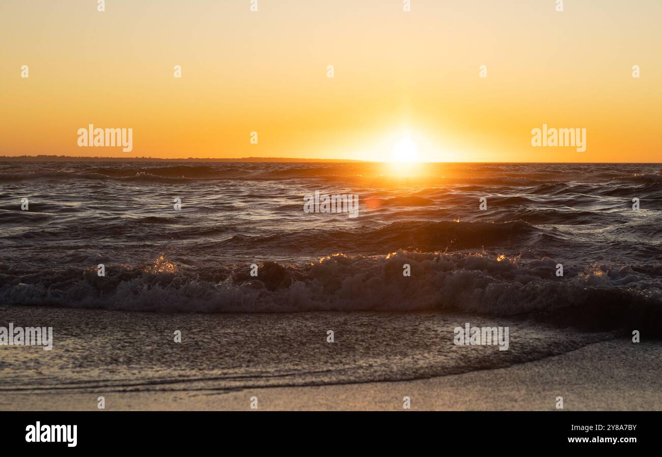 Pittoresco paesaggio di mare calmo e onde sulla spiaggia sul tramonto e il cielo arancione Foto Stock