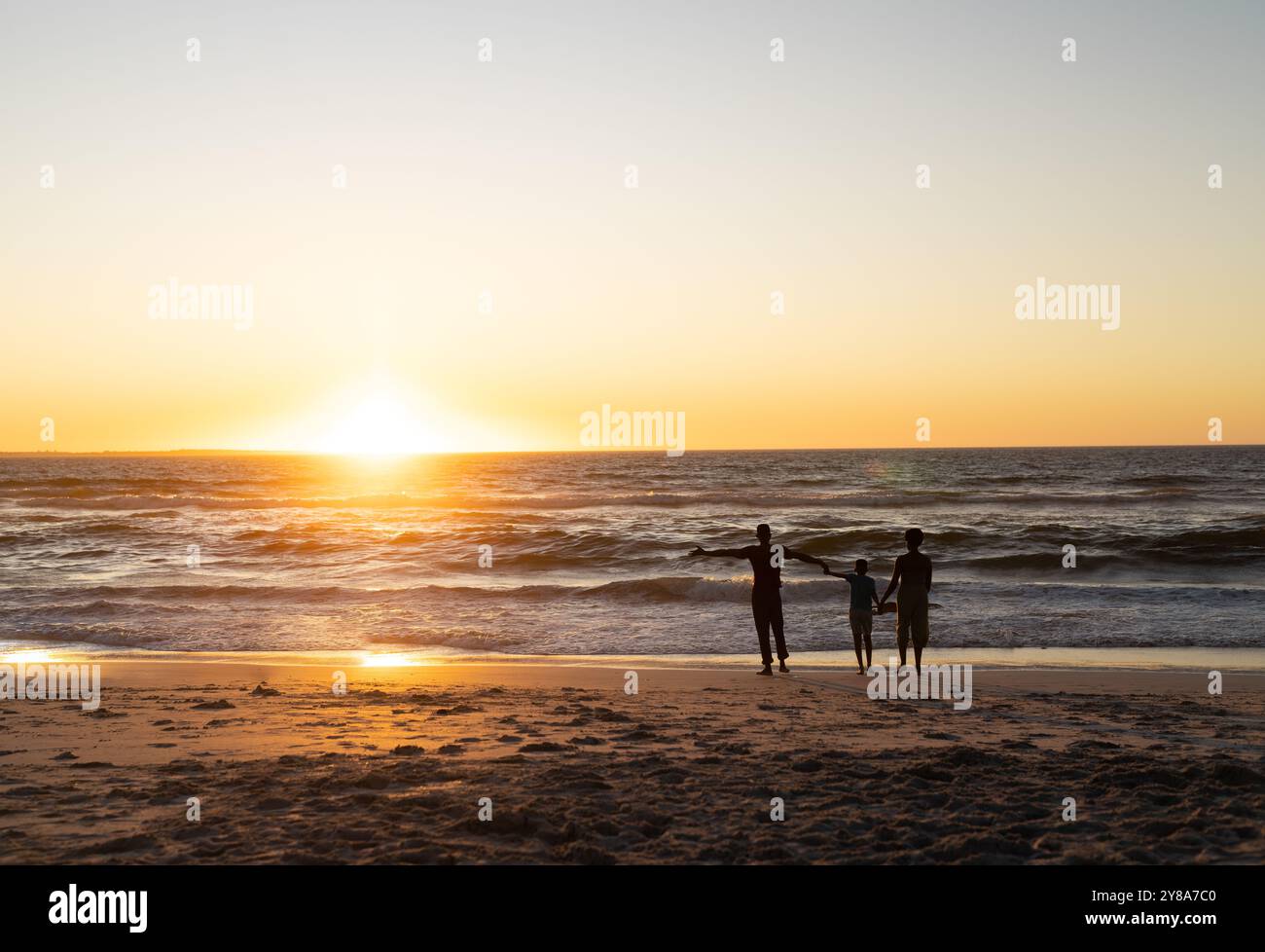 Silhouette figlio afroamericano che tiene le mani di madre e padre e si trova sulla spiaggia al tramonto Foto Stock