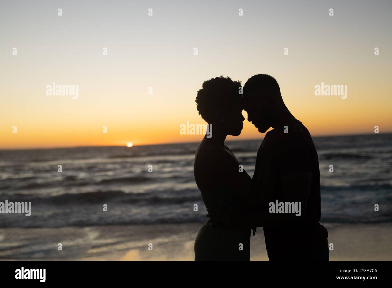 Silhouette coppia afroamericana romantica con testa a testa in piedi in spiaggia durante il tramonto Foto Stock