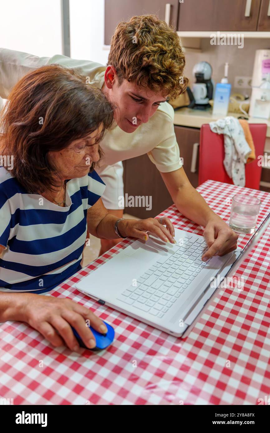 Adolescente che insegna alla nonna di 70 anni a utilizzare un notebook, colmando il divario digitale Foto Stock