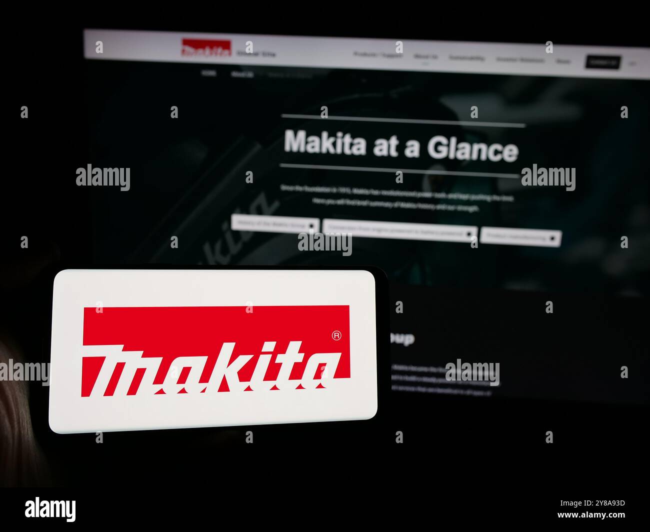 Persona che possiede uno smartphone con il logo dell'azienda giapponese Makita Corporation sullo schermo di fronte al sito Web. Mettere a fuoco il display del telefono. Foto Stock