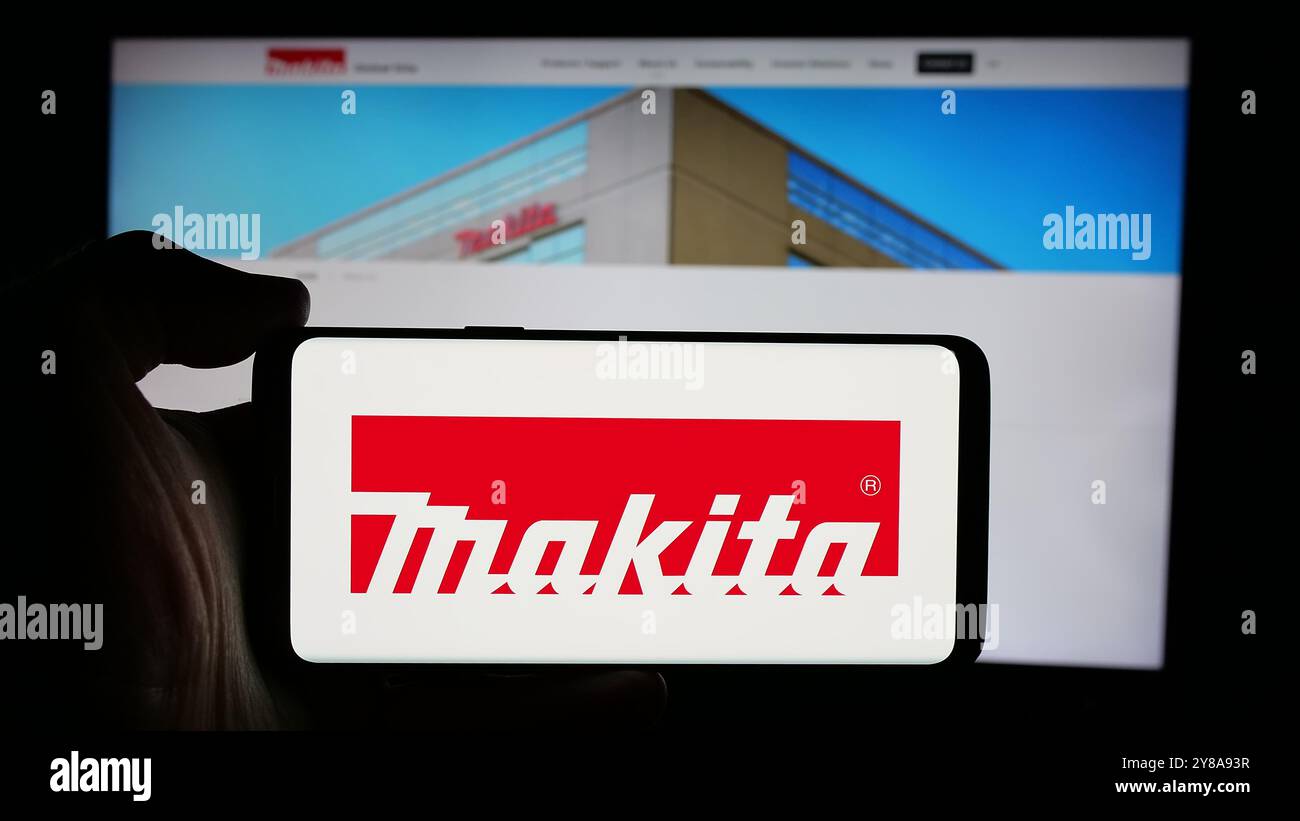 Persona che detiene un cellulare con il logo della società giapponese di utensili elettrici Makita Corporation sullo schermo davanti alla pagina Web. Mettere a fuoco il display del telefono. Foto Stock