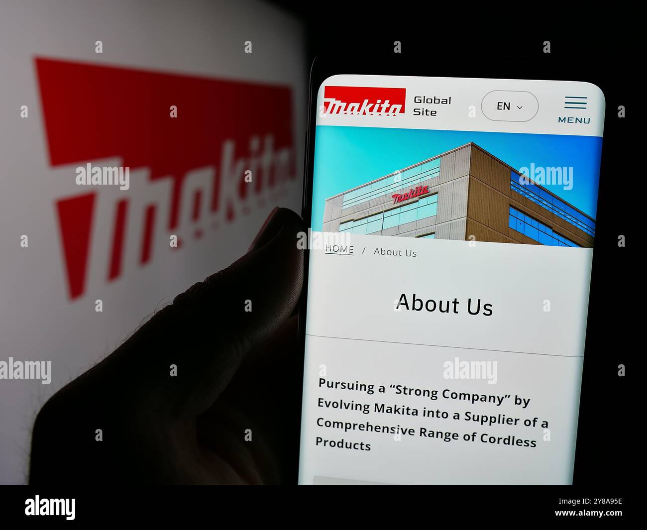 Persona che tiene un cellulare con il sito web della società giapponese di utensili elettrici Makita Corporation sullo schermo con il logo. Messa a fuoco al centro del display del telefono. Foto Stock