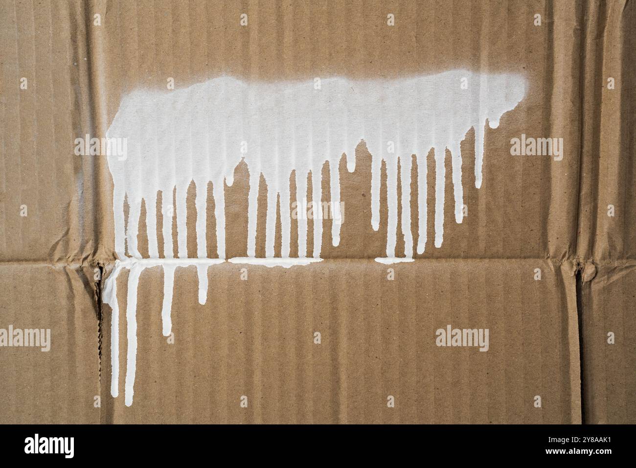 Una striscia di vernice spray bianca con gocciolamenti su un cartone Foto Stock
