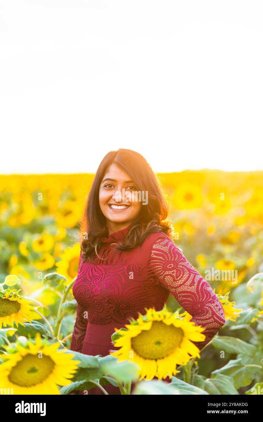 Donna sorridente in piedi in un campo di girasoli durante l'ora d'oro al tramonto. Foto Stock