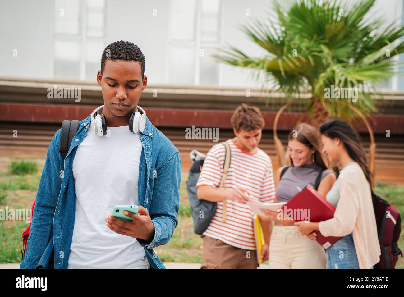Serio studente afroamericano che usa un cellulare nel campus universitario. Tizio isolato che guarda cattive notizie sul suo smartphone al liceo. Giovane uomo in piedi con un telefono cellulare fuori. Foto di alta qualità Foto Stock
