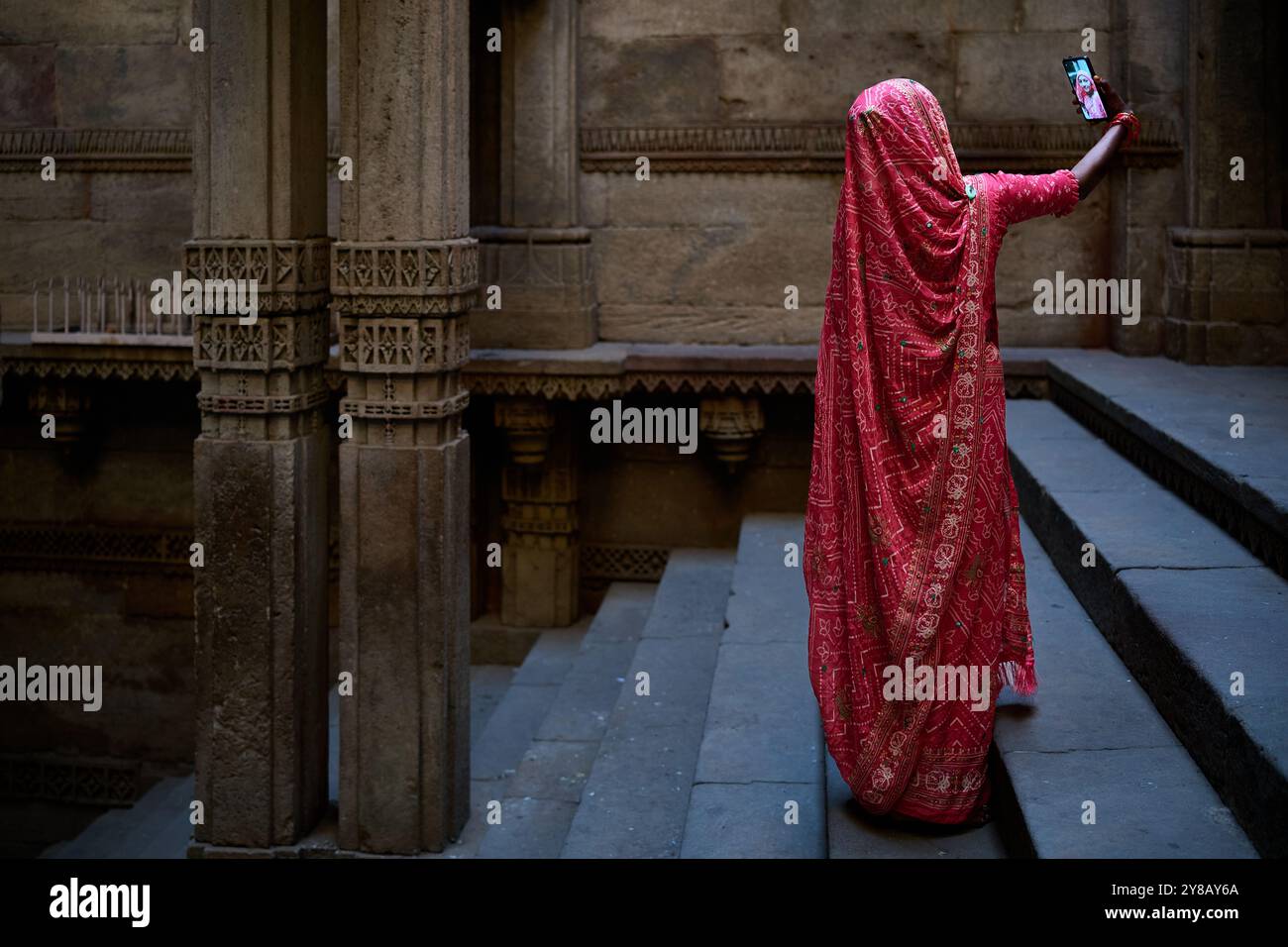 Una donna in un tradizionale sari rosa scatta una foto con uno smartphone sui gradini dello storico gradino di Adalaj in India Foto Stock