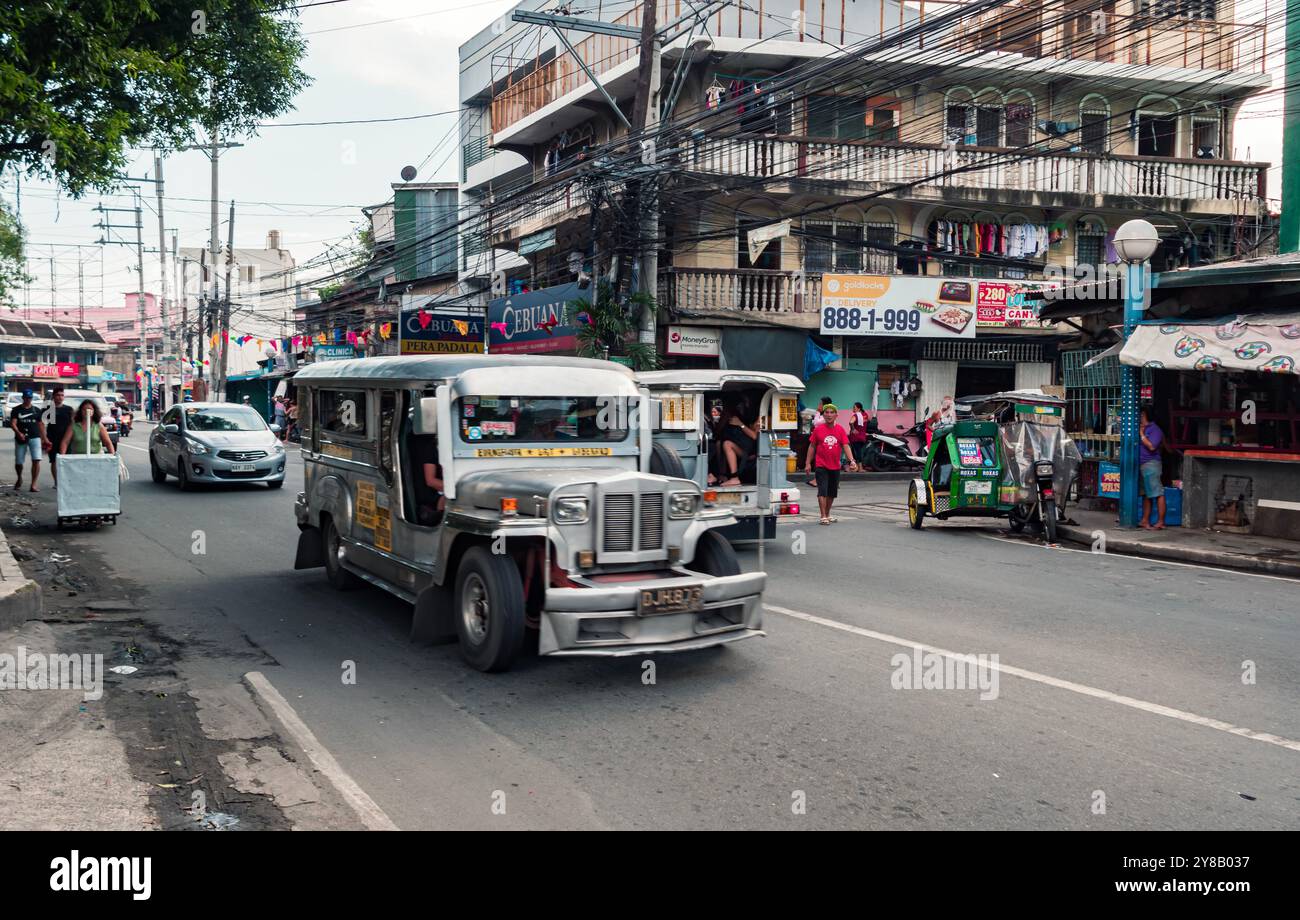 Manila, Filippine - 26 agosto 2019: Una vivace jeepney percorre una strada trafficata piena di negozi e pedoni. Foto Stock