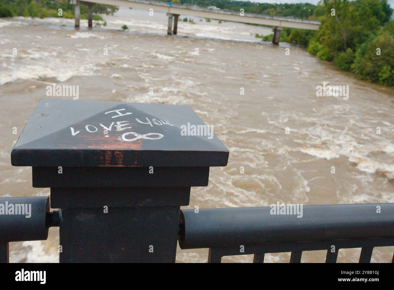 Ampia vista su piedistallo nero, parole i Love You scritte a mano in bianco a sprofondare fangosa argilla marrone flusso d'acqua che rotola con tappi bianchi. Foto Stock