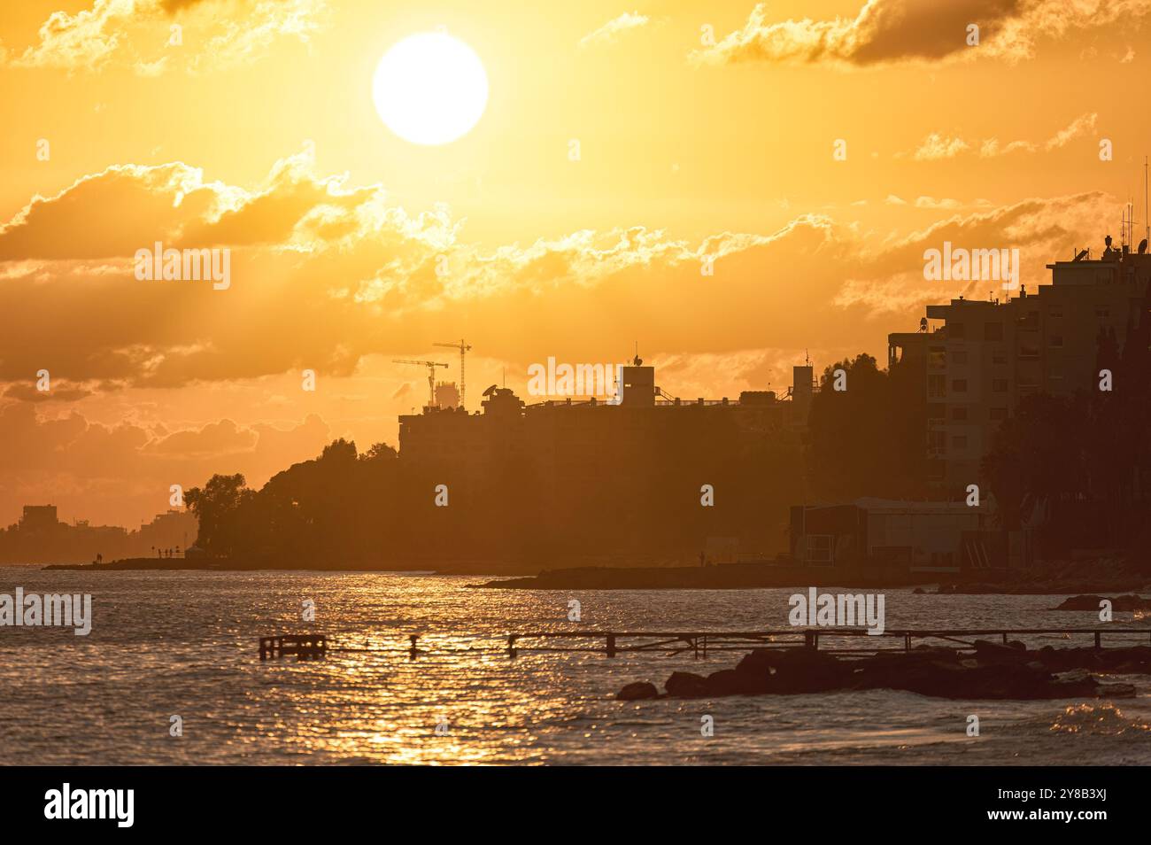 Tramonto dorato luminoso sullo skyline della città di Limassol, Cipro, con gru da costruzione in lontananza Foto Stock