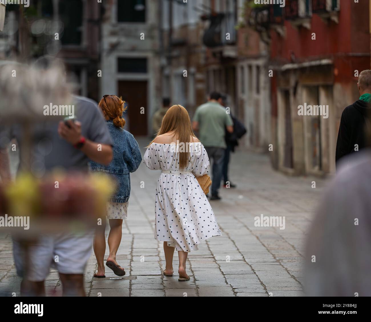 Vista posteriore di una donna in abito bianco con pois neri in una strada a Venezia, Italia. Turisti che camminano lungo una stradina stretta di Venezia. Foto Stock