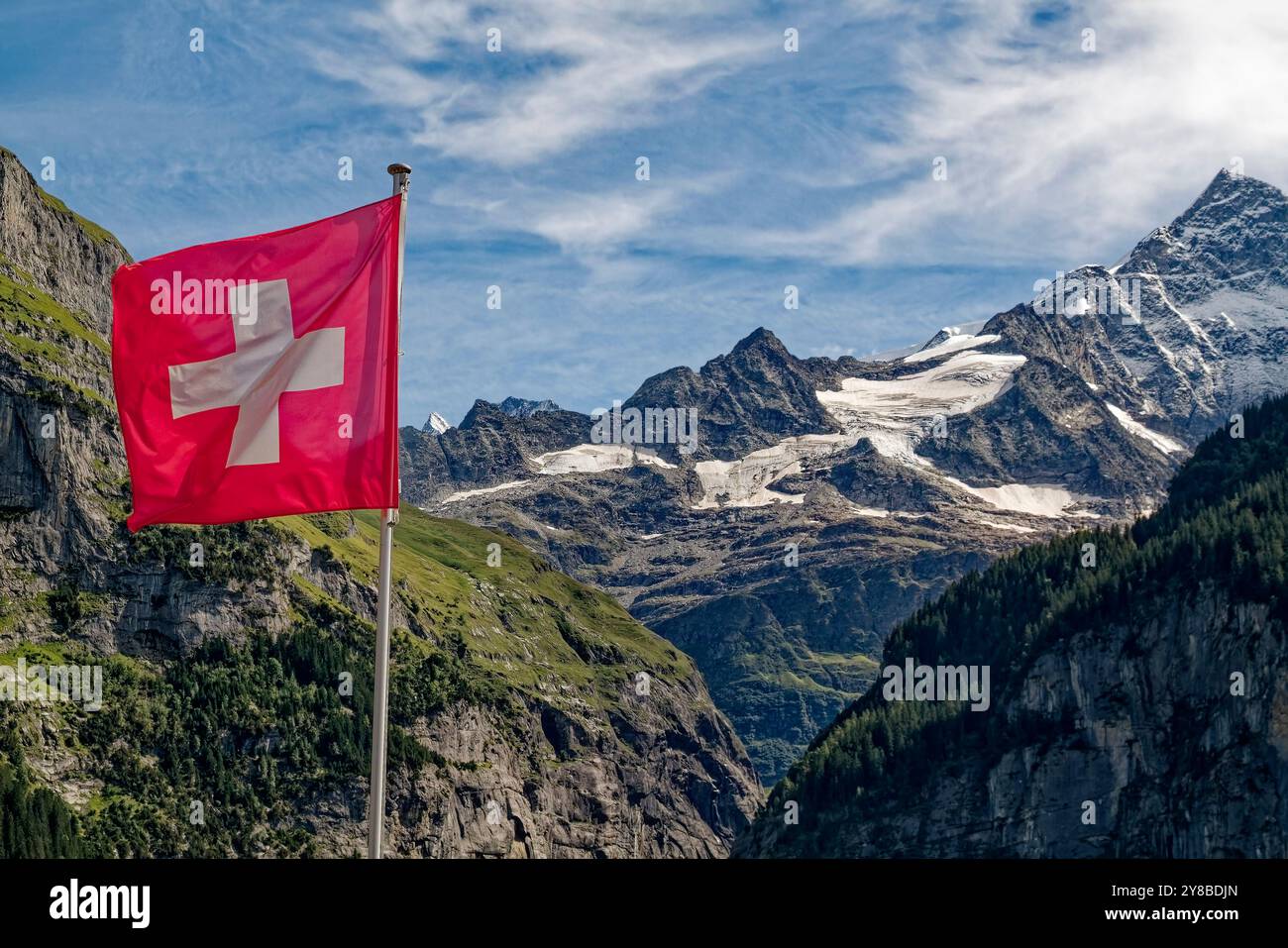 Bandiera svizzera, sfondo rosso, croce bianca, montagne, macchie di neve, nuvole insolite, Alpi, Europa, Grindelwald, Svizzera, estate Foto Stock