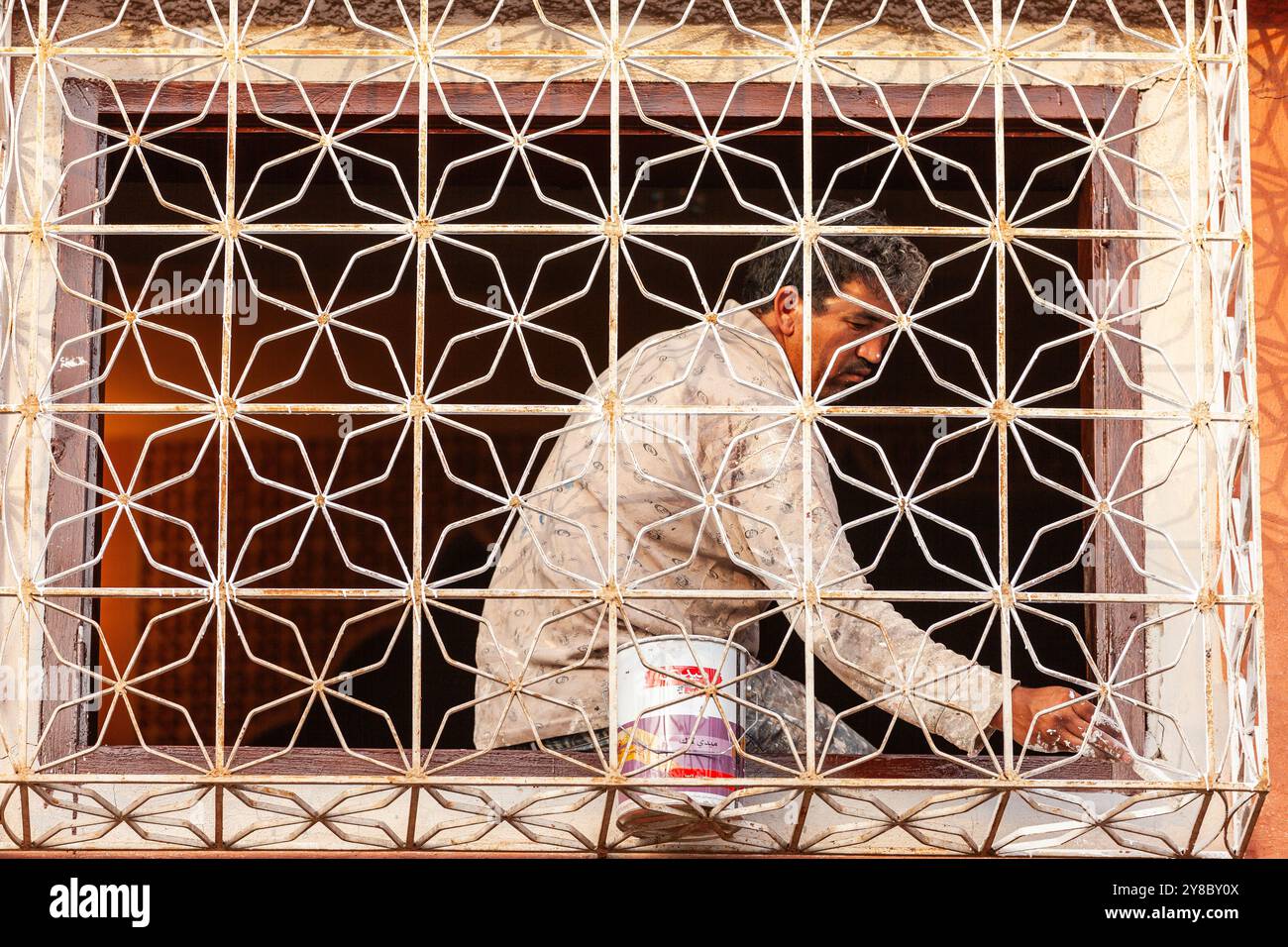 Dietro un cancello in ferro battuto che protegge una finestra, un uomo completa un lavoro di pittura. Foto Stock