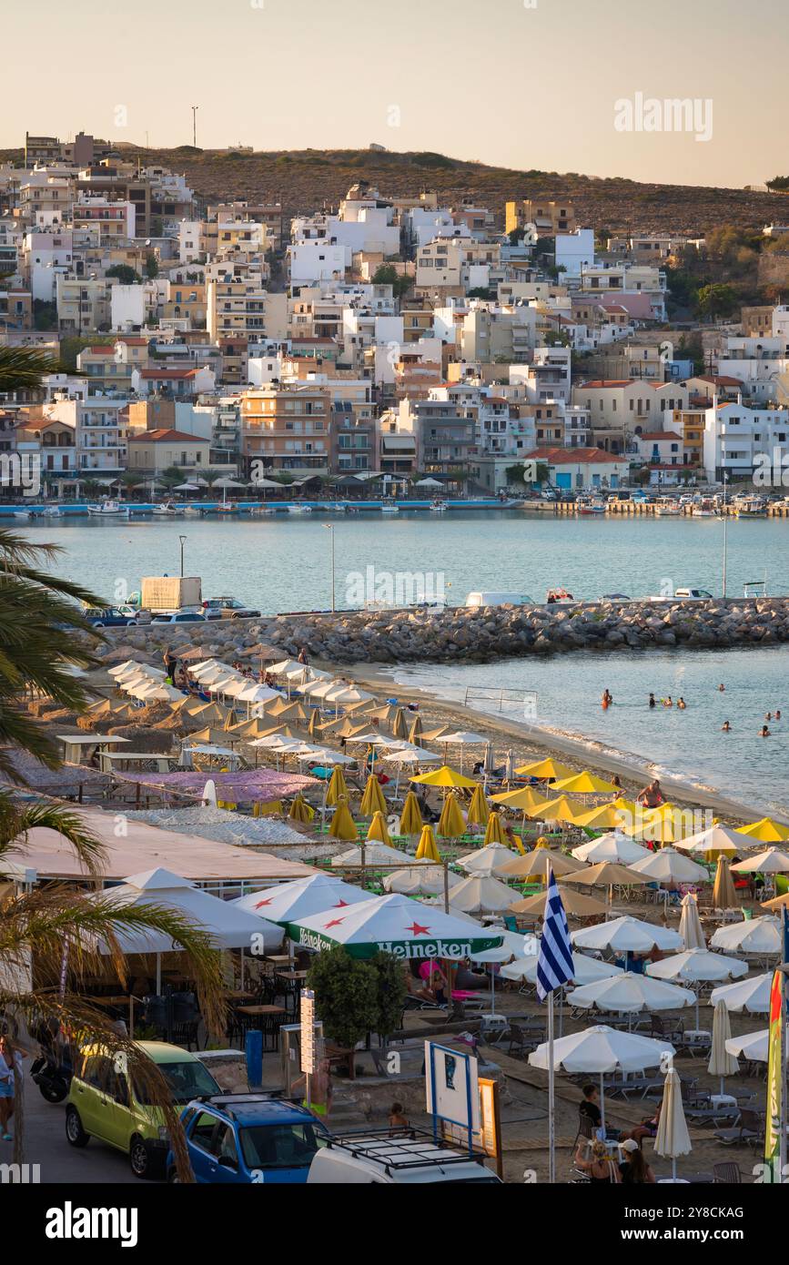 Spiaggia della città di Sitia, vista delle persone che si godono del tempo sulla spiaggia di Sitia Bay, mostrando la città vecchia di Sitia di fronte alla baia, Lasithi, Creta, Grecia Foto Stock
