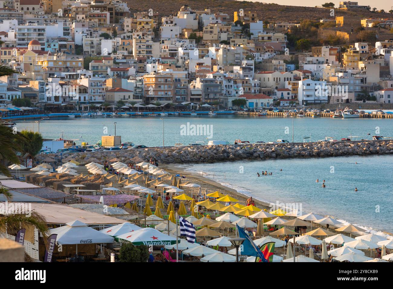 Spiaggia della città di Sitia, vista delle persone che si godono del tempo sulla spiaggia di Sitia Bay, mostrando la città vecchia di Sitia di fronte alla baia, Lasithi, Creta, Grecia Foto Stock
