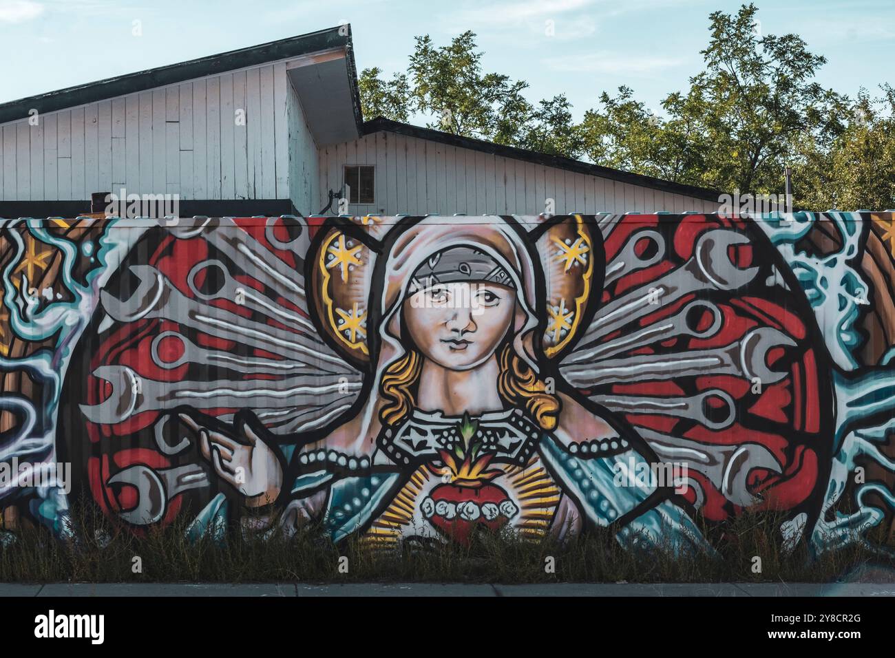 Un murale della Vergine Maria e strumenti meccanici, dipinto su una recinzione metallica a Ojo Caliente, New Mexico, USA Foto Stock