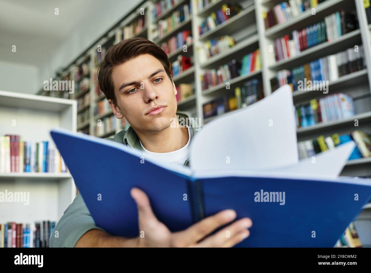 Uno studente dedicato si concentra intensamente sui suoi studi in una biblioteca ben fornita. Foto Stock