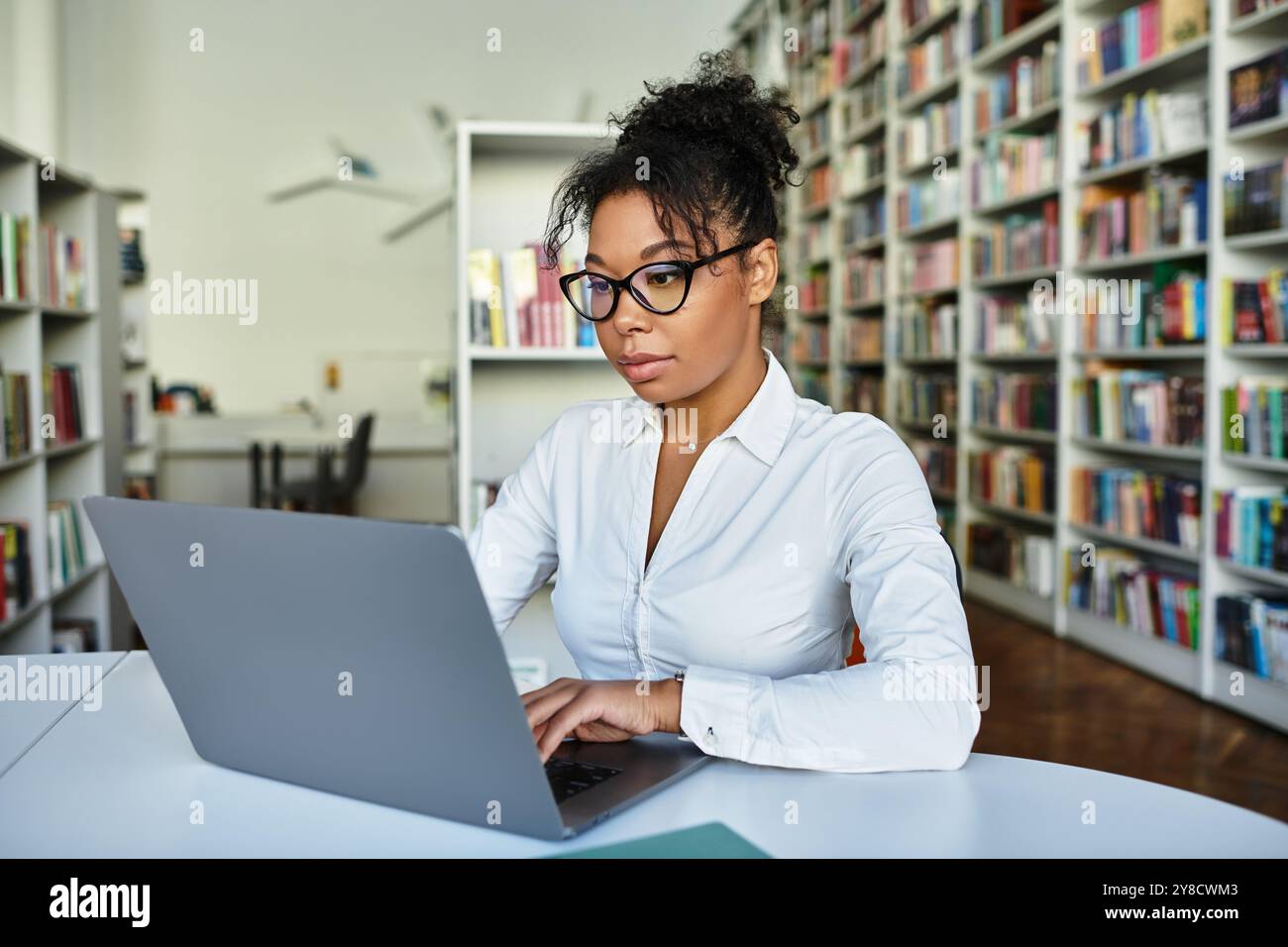 Un insegnante afroamericano specializzato utilizza un laptop in una vivace libreria per migliorare l'apprendimento. Foto Stock