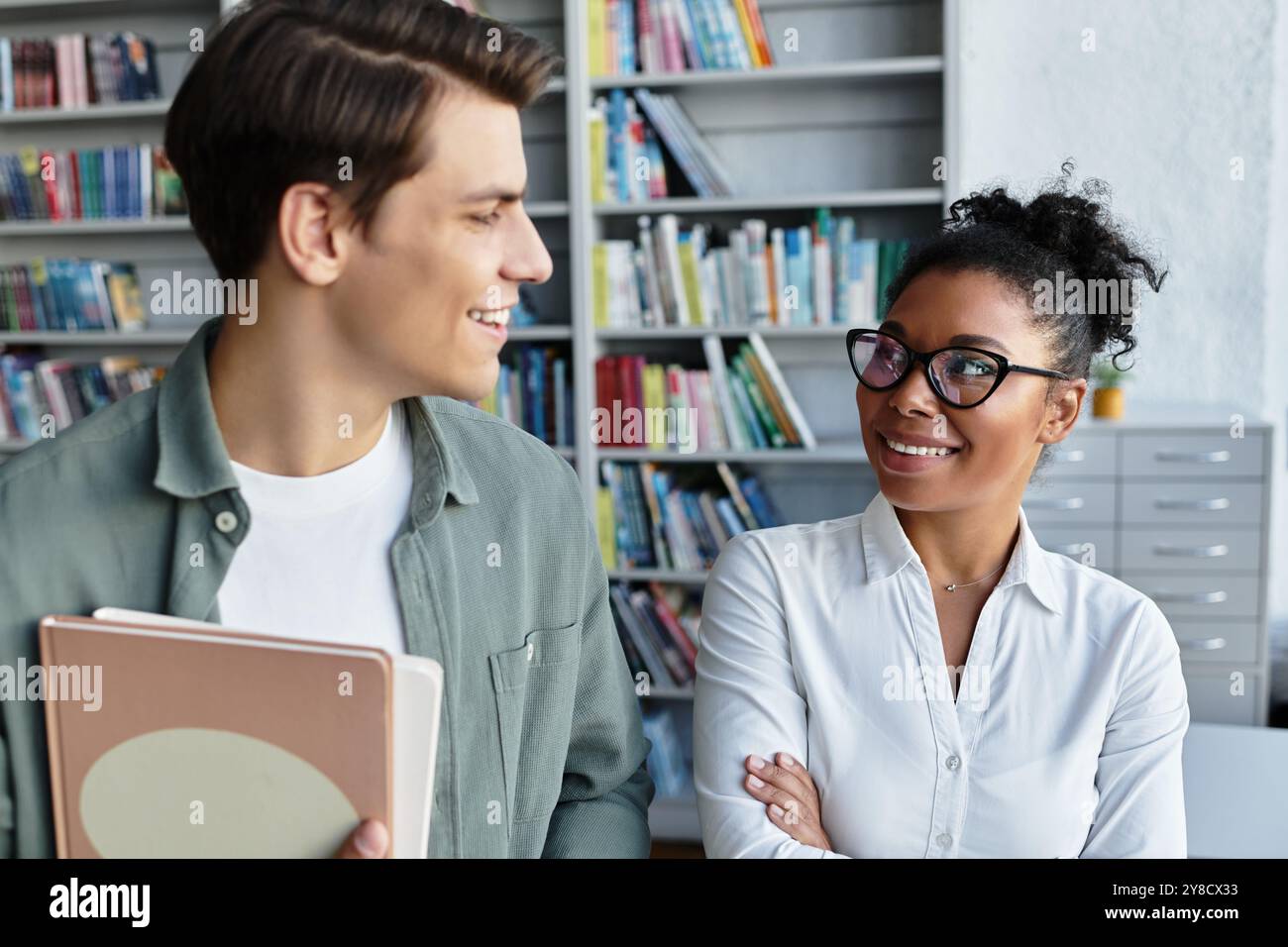 In una vivace biblioteca, un insegnante dedicato coinvolge il suo studente curioso, stimolando l'apprendimento. Foto Stock