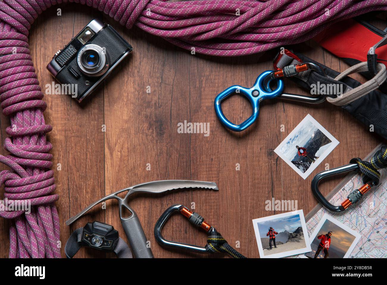 Vista dall'alto del tavolo in legno con attrezzatura per arrampicata, fune, moschettoni, ascia ghiacciata, mappa, faro, coltello tascabile, notebook e fotocamera d'epoca con foto di m Foto Stock
