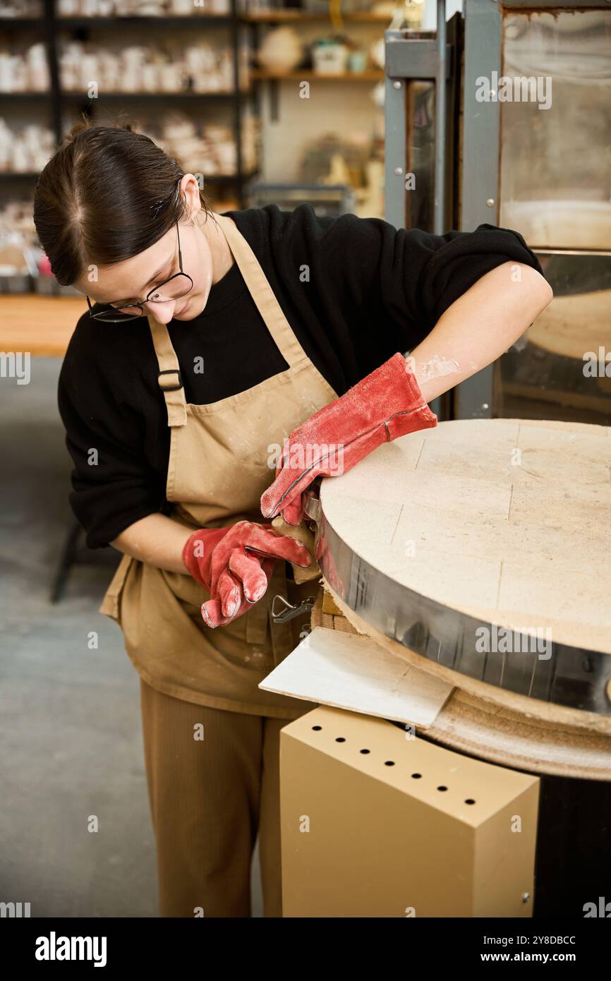 Donna con guanti da lavoro rossi lavora in uno studio di ceramica Foto Stock