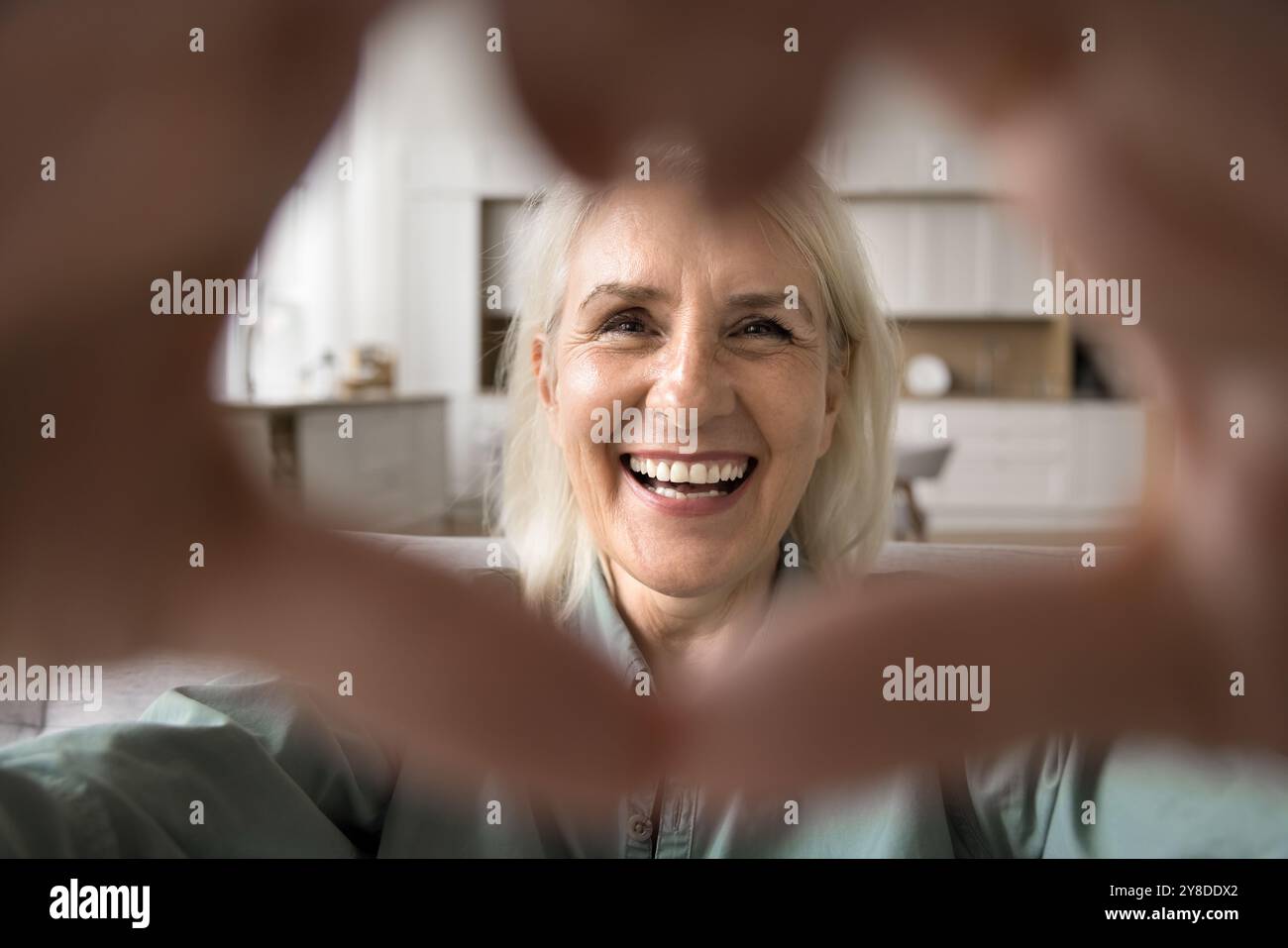Una donna anziana guarda la macchina fotografica a forma di cuore con le mani Foto Stock