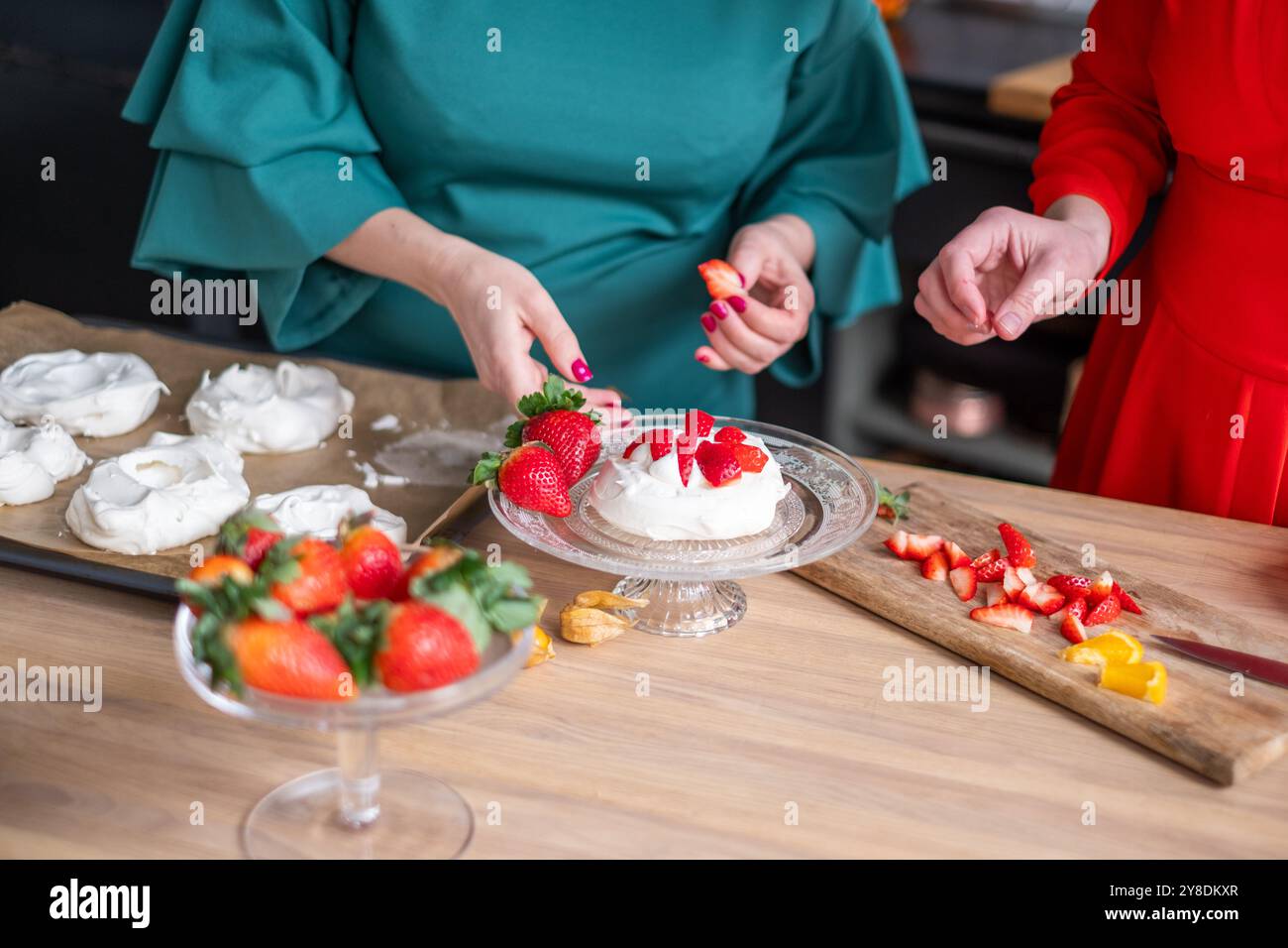 In cucina, le donne decorano le meringhe con fragole fresche, mettendo in mostra il lavoro di squadra e la creatività, il vivace concetto di colori culinari Foto Stock