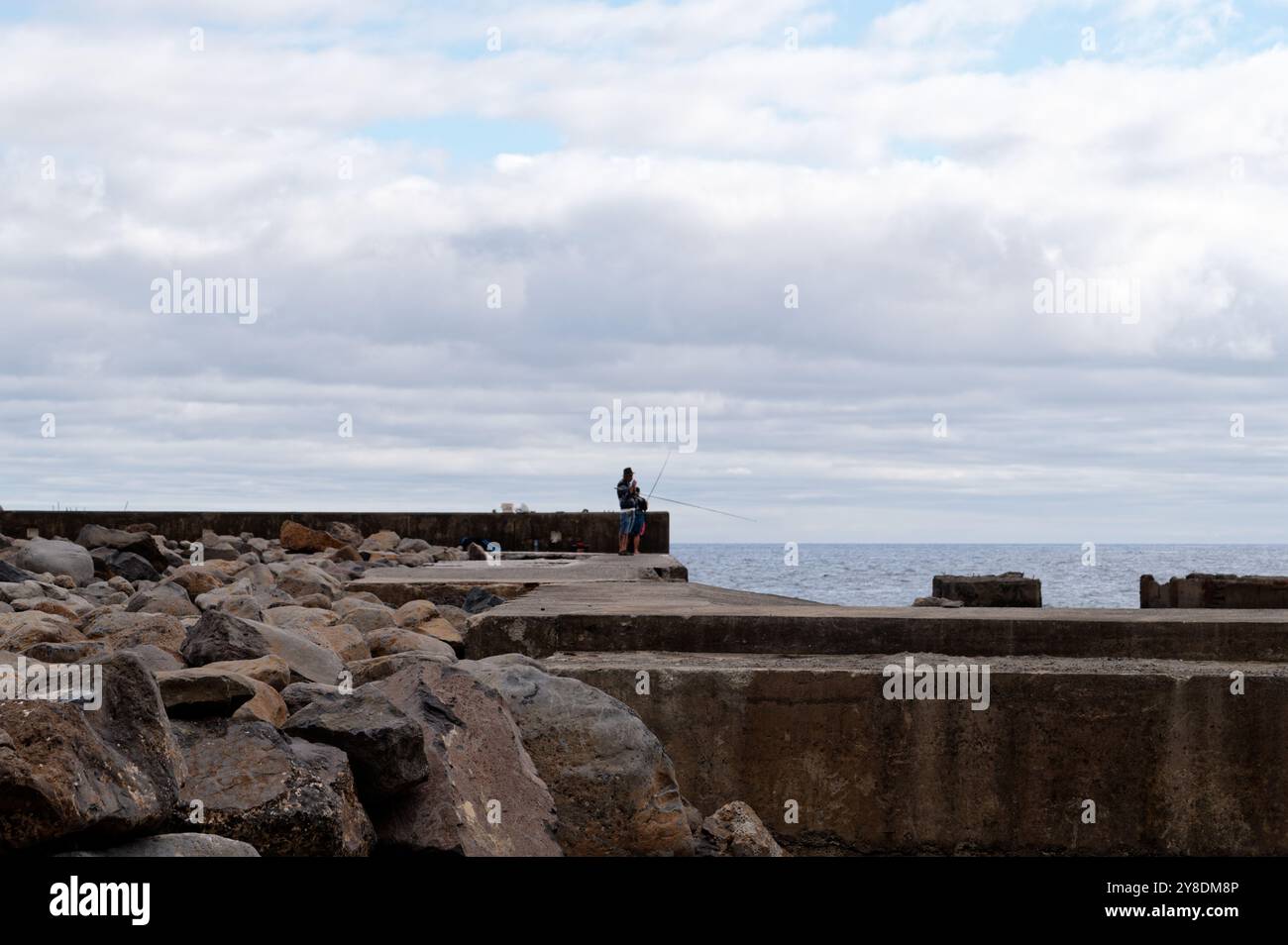 Figura solitaria che pesca da un molo roccioso con calme vedute dell'oceano a Madeira Foto Stock