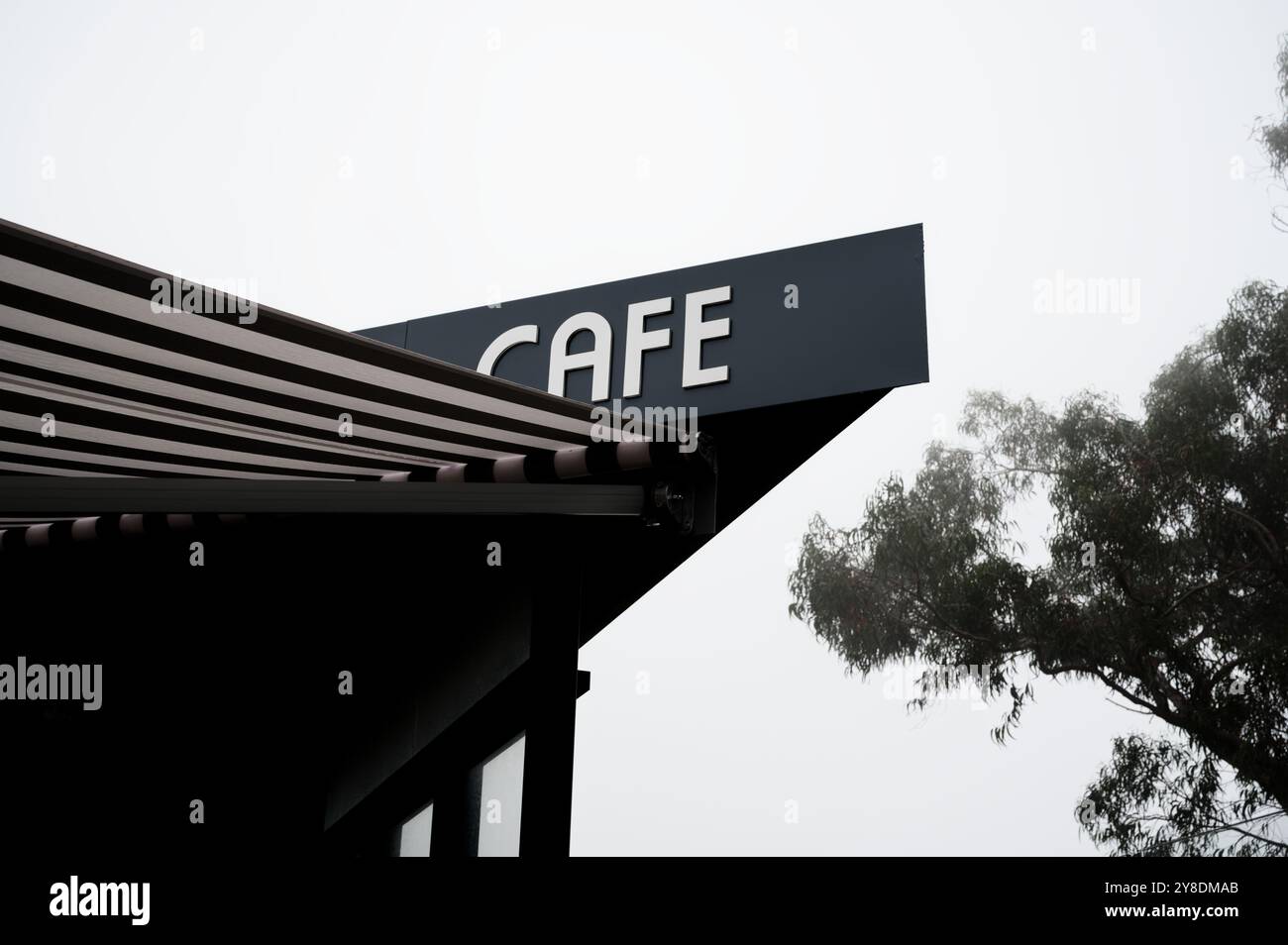 Moderno cartello da caffe' su un cielo nebbioso con sagome di alberi sullo sfondo Foto Stock
