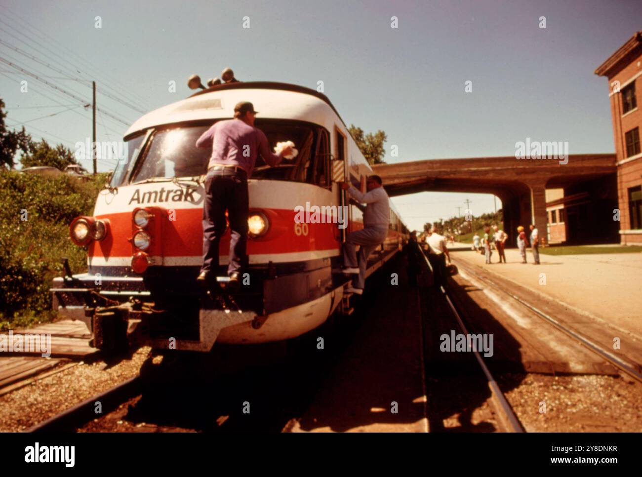 Il parabrezza del motore Turboliner viene pulito mentre il treno passeggeri si ferma a Bloomington, Illinois, in viaggio da St. Louis, Missouri, a Chicago. Il treno costruito in Francia è in grado di raggiungere velocità fino a 125 miglia all'ora, ma normalmente non viaggia più velocemente di 79 miglia all'ora su questa corsa. Molti dei treni passeggeri nel sistema Amtrak funzionano più lentamente delle loro capacità perché le ferrovie della nazione hanno bisogno di aggiornare binari e piazzole, giugno 1974. Foto Stock