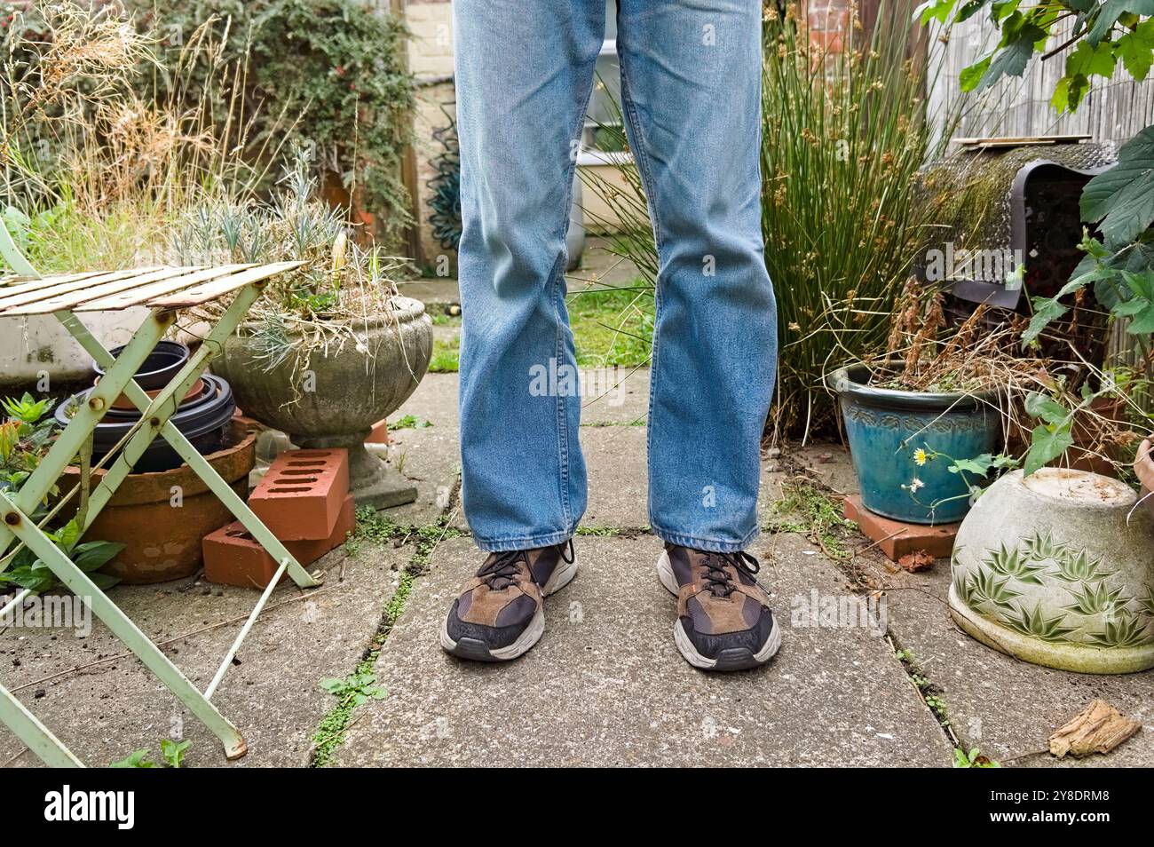 gambe e piedi di un uomo che indossa jeans e scarpe da ginnastica e si trova in giardino Foto Stock