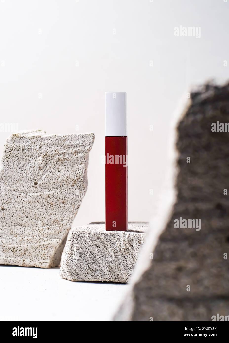 Un sorprendente tubo rosso del rossetto elegantemente esposto su uno sfondo di pietra bianca testurizzata. Questa fotografia minimalista mette in risalto i colori audaci e la S Foto Stock