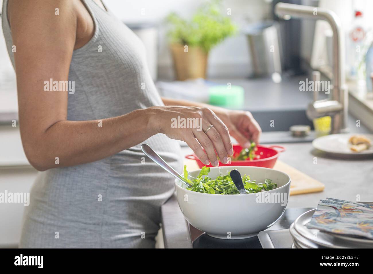 Una donna incinta prepara insalata verde fresca in una cucina moderna Foto Stock