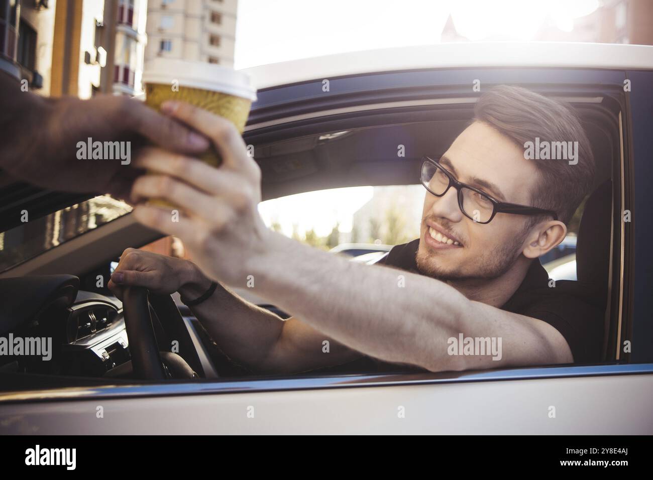 Giovane uomo sorridente che guida l'auto e prende via il caffè Foto Stock