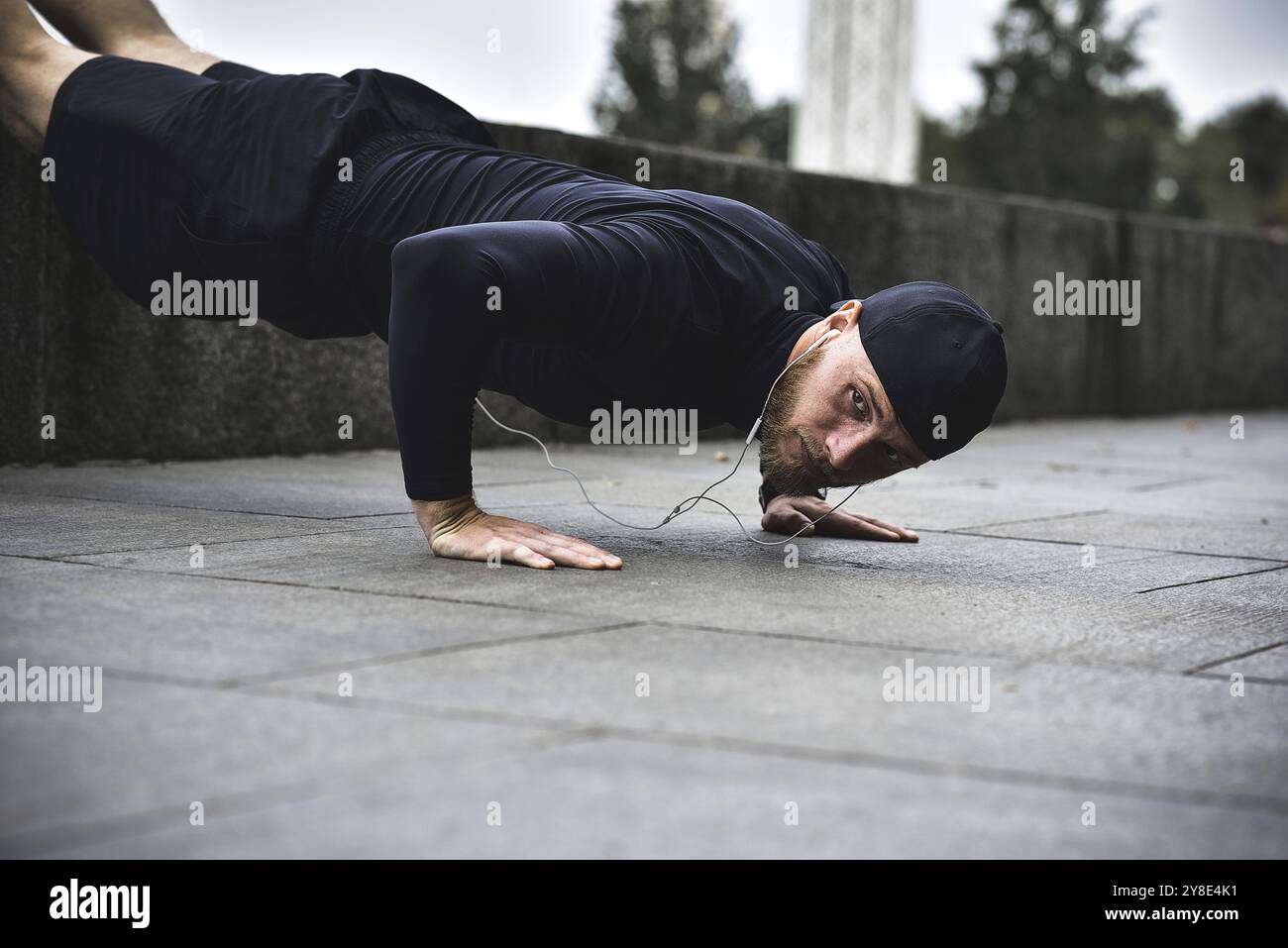 Il giovane sportivo con barba si allena in un parco, facendo una serie di push up all'aperto Foto Stock