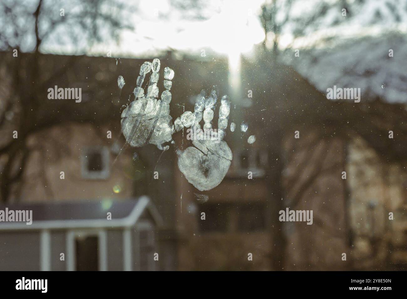 Impronte digitali su una finestra alla luce del sole con case sullo sfondo Foto Stock