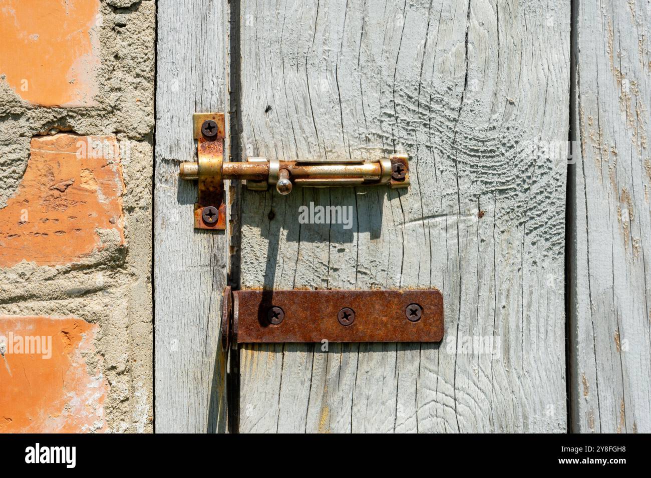 Vecchia porta in legno con serratura metallica arrugginita sullo sfondo di una parete in mattoni usurati Foto Stock