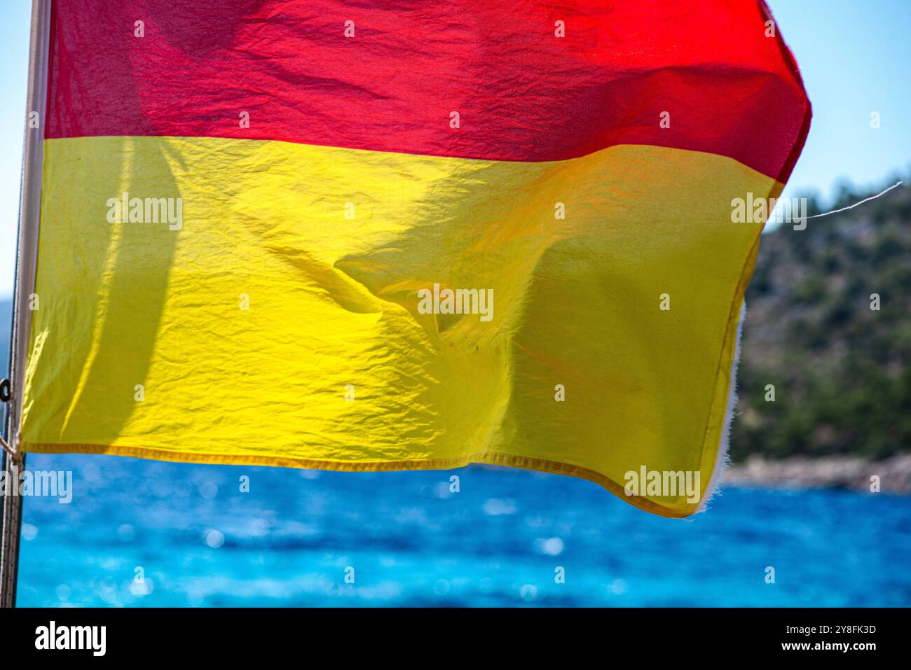 Uno scatto ravvicinato di una bandiera bagnino che fluttua nel vento su una spiaggia sabbiosa, simboleggia la sicurezza e la vigilanza con il vibrante sfondo marino. Foto Stock
