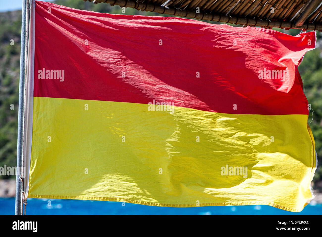 Uno scatto ravvicinato di una bandiera bagnino che fluttua nel vento su una spiaggia sabbiosa, simboleggia la sicurezza e la vigilanza con il vibrante sfondo marino. Foto Stock