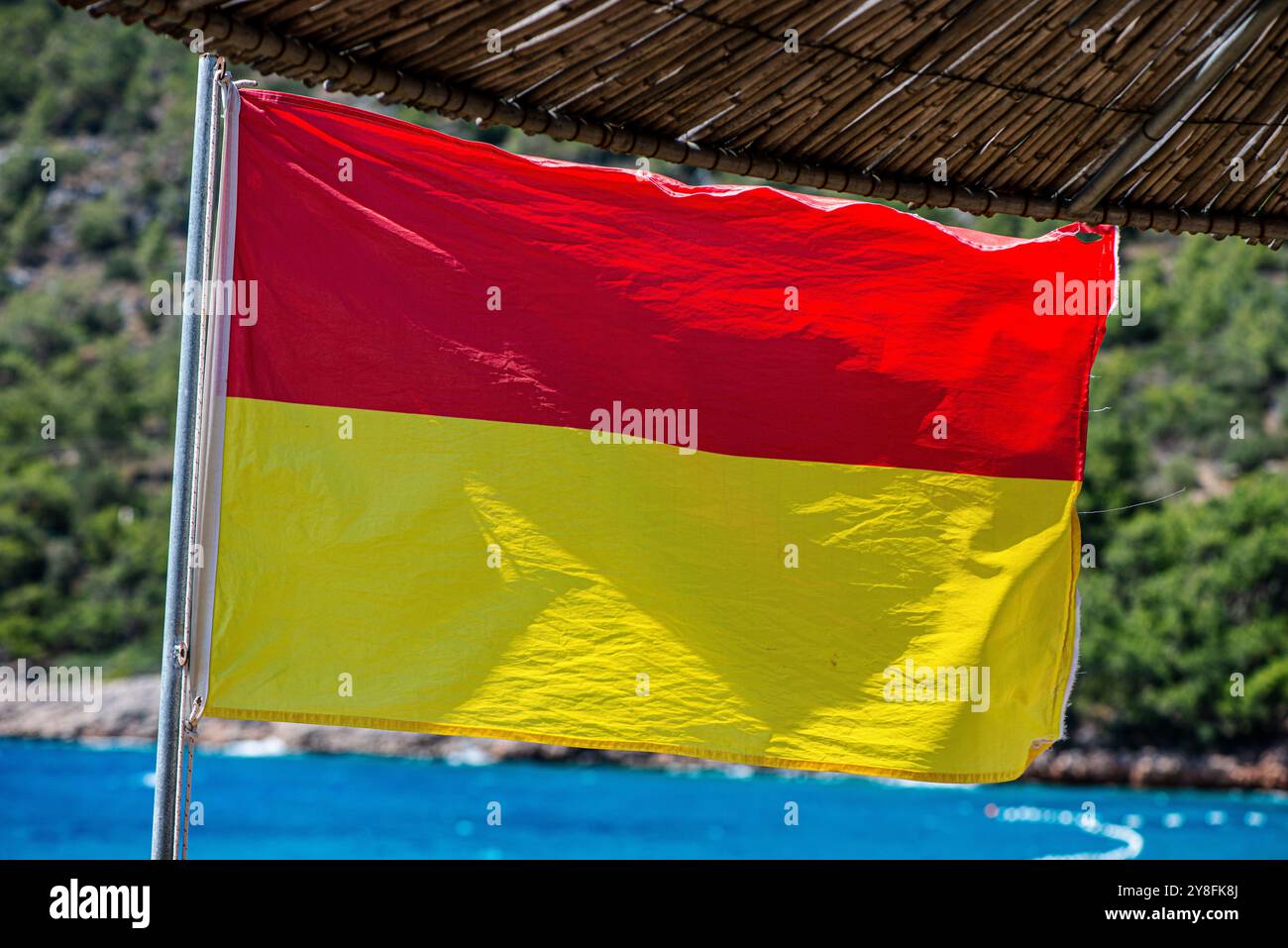 Uno scatto ravvicinato di una bandiera bagnino che fluttua nel vento su una spiaggia sabbiosa, simboleggia la sicurezza e la vigilanza con il vibrante sfondo marino. Foto Stock